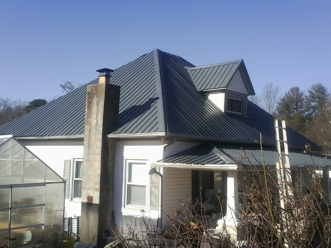 Dark blue standing seam metal roof on a white farmhouse with dormer — Slate & Tile Roof Repair by Roofing Brothers in Kendleton
