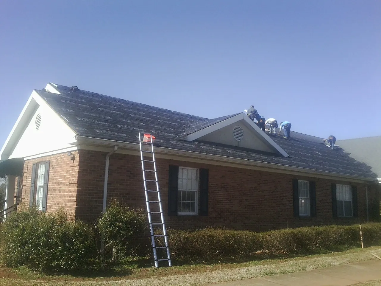 Crew tearing shingles off a brick ranch roof with a ladder set — Emergency Roof Repair work by our crew in Kendleton