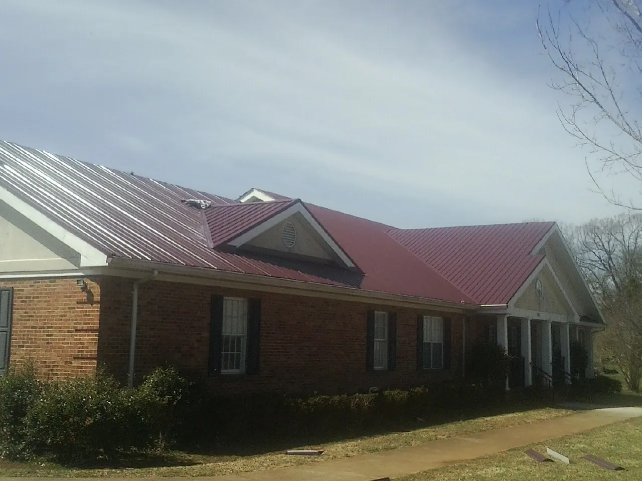 Red metal roof with gabled entries on a long brick building, from a Hail Damage Roof Repair job in Kendleton