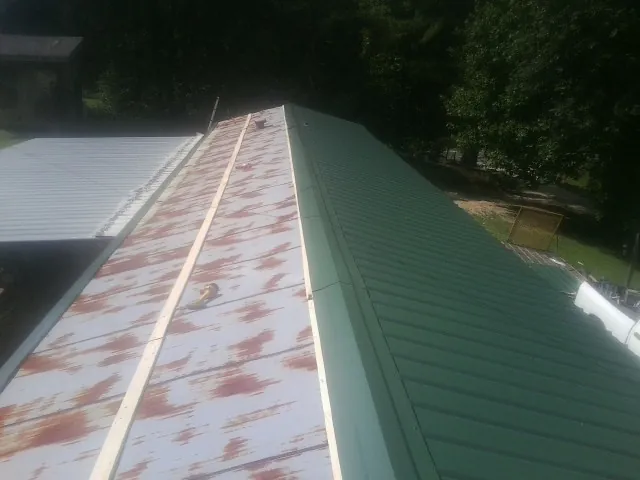 Old rusted panels beside newly installed green metal roofing — Wind Damage Roof Repair by Roofing Brothers in Kendleton