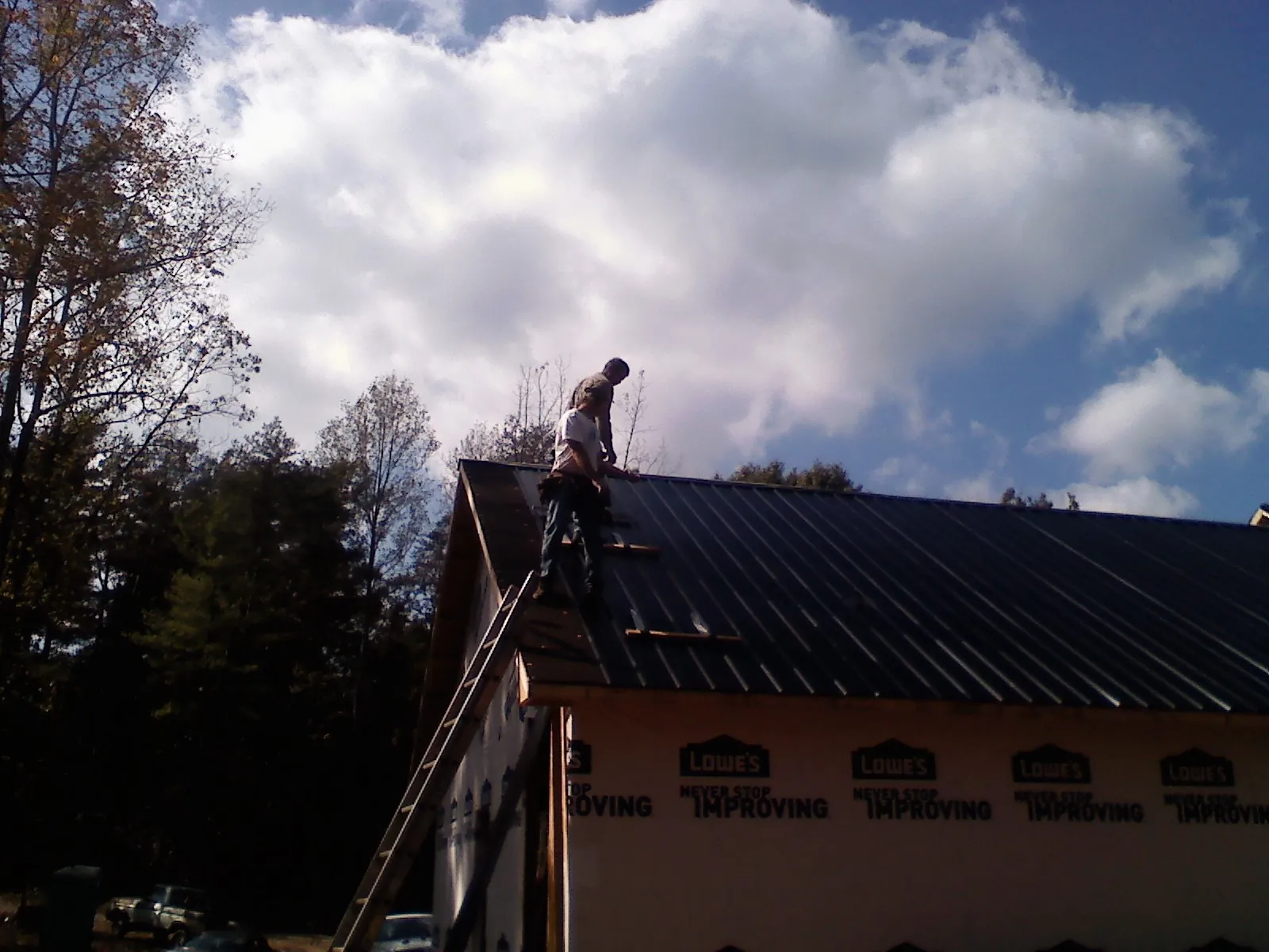Roofer fastening dark metal panels high against a cloudy sky, from a Roof Inspection job in Kendleton