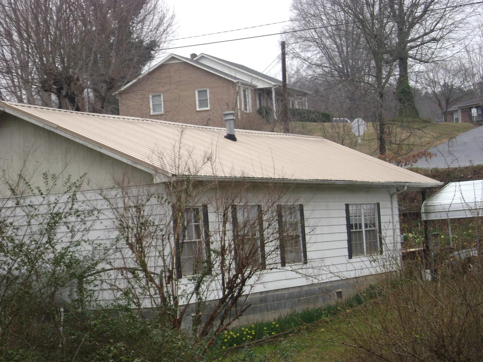 Tan metal roof on a white sided house set into a hillside — Commercial Roofing by Roofing Brothers in Kendleton